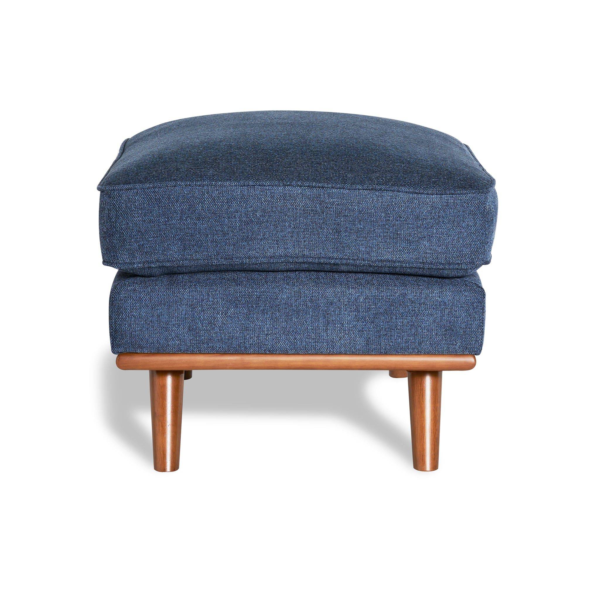 The Maddox Ottoman features a rectangular cushion in blue upholstery and rests elegantly on wooden legs, casting a shadow against a white background—ideal for adding mid-century charm to any living space.