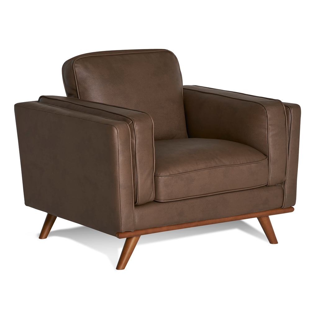The Maddox Chair, with a mid-century modern design, features plush cushions, clean lines, padded armrests, and angled wooden legs in brown leather, set against a plain white background.