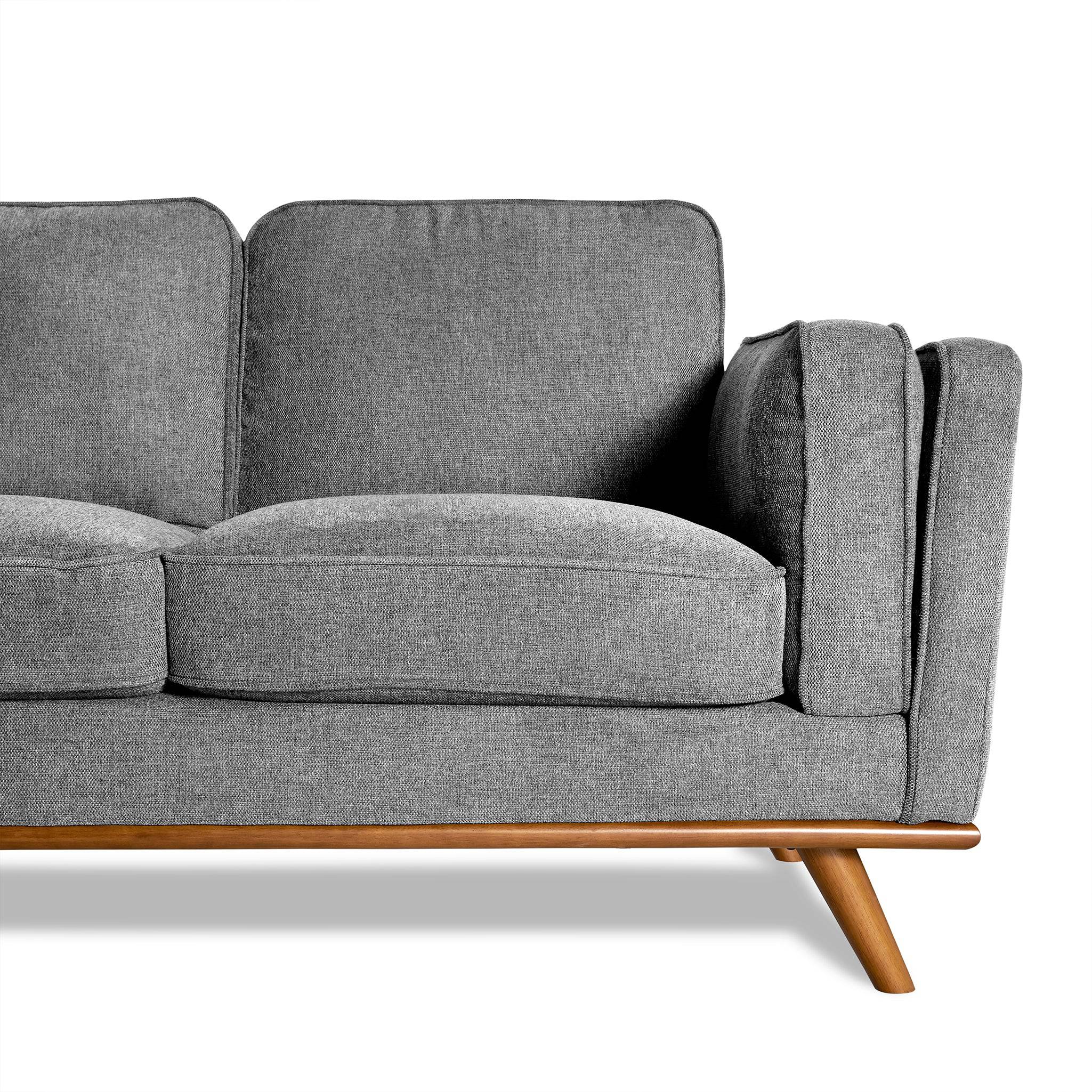 The Maddox is a modern gray fabric sofa with a wooden base and angled legs. It features plush cushions and an armrest, embodying mid-century modern design against a white background, perfect for any living room.