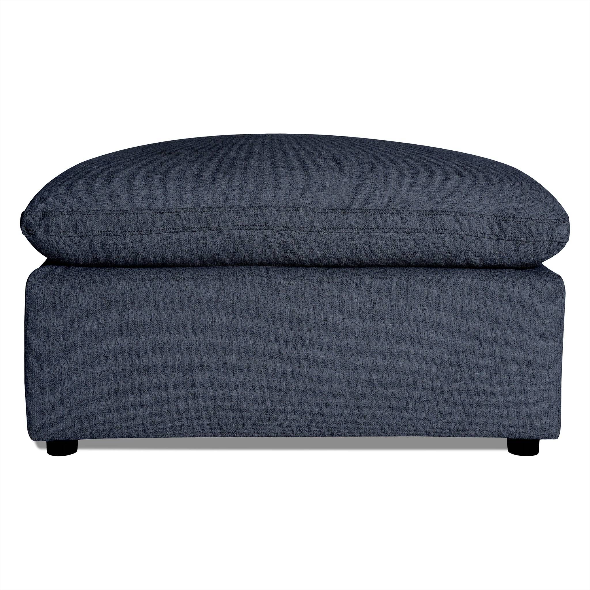 The My Cloud 40 Ottoman features dark gray upholstery with a soft cushioned top and short black legs. Its textured fabric adds to the modern, minimalist design, making it an ideal customizable piece for any living room.